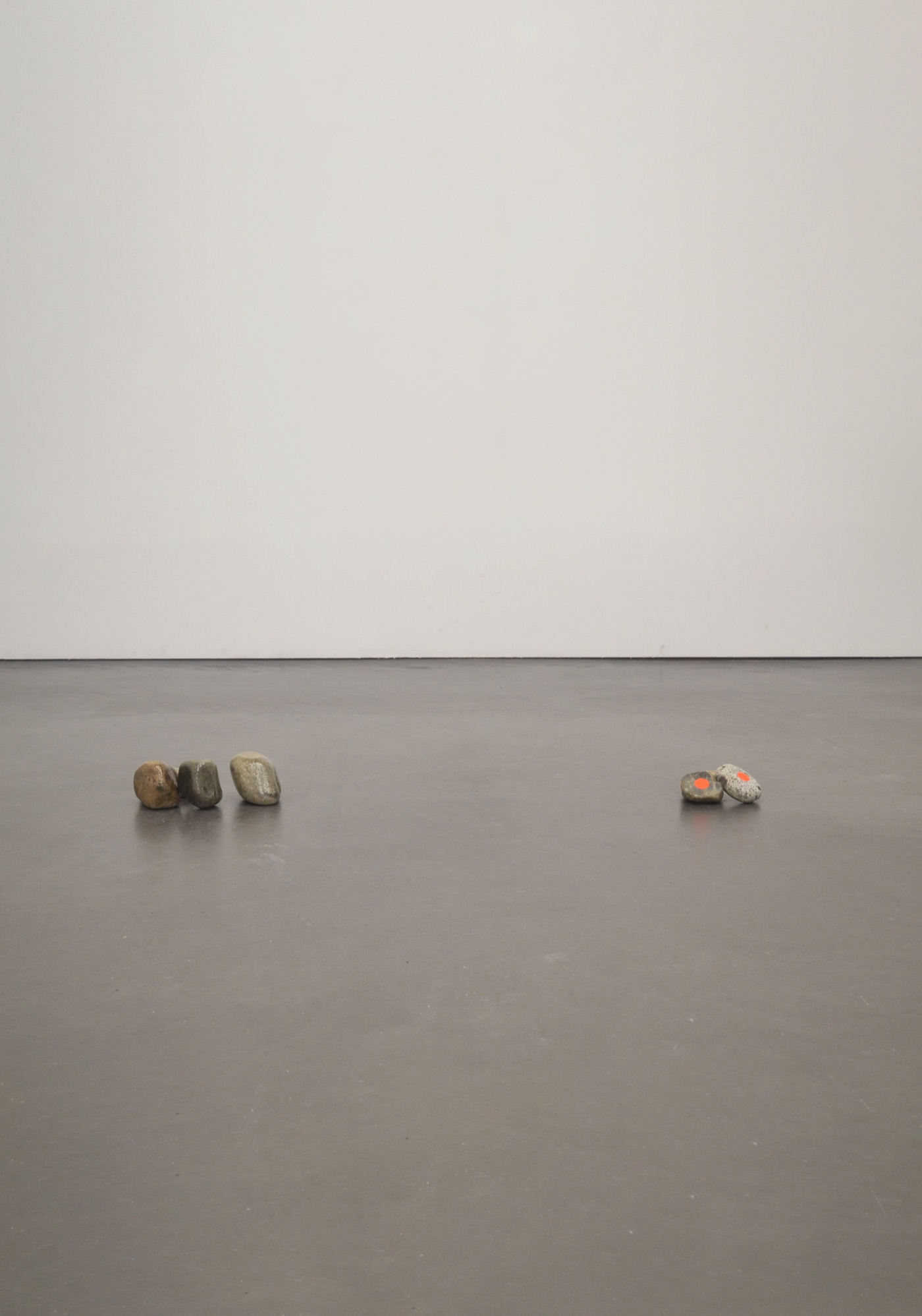 Deux groupes de cailloux posés au sol dans une salle d’exposition blanche